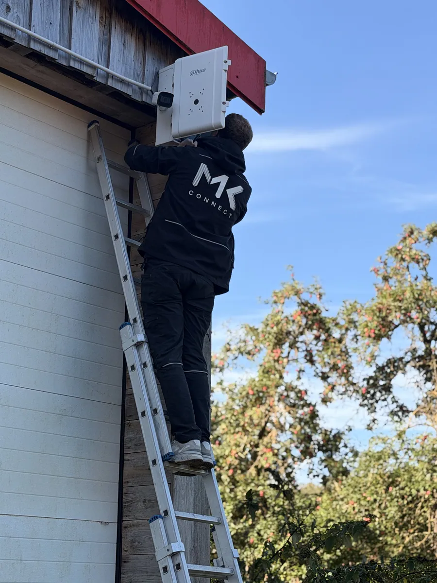 Technicien MK Connect pendant l'entretien d'une caméra sous l'avant-toit d'un bâtiment à Rots